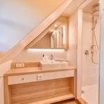 Bathroom with shower, sink, and mirror under sloped ceiling.