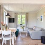 Living and dining area with sofa, dining table, and windows. Wooden floor and ceiling beams.