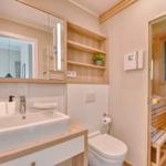 Bad mit Waschbecken, Spiegel und Sauna im Hintergrund.