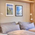 Schlafzimmer mit Bett, Kissen und Wandbildern. Beleuchtung und Pflanze sichtbar.