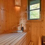 Sauna mit Holzwand, Sitzbank, Eimer und Fenster zur Natur.