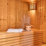Sauna mit Holzwand, Holzbank, Handtuch, Eimer und Öle.