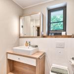 Badezimmer mit Waschtisch, Spiegel und Fenster mit Blick auf Grün.