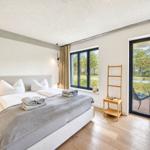Schlafzimmer mit Doppelbett, Holzboden und Blick auf Pool und Garten.