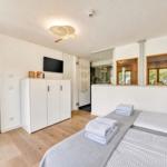 Zimmer mit Doppelbett, Kleiderschrank und TV. Durchgang zur Sauna und Wohnbereich.
