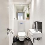 Dusche mit modernem Waschbecken und Toilette. Schwarze Fliesen und Spiegel.