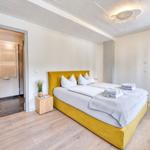 Schlafzimmer mit gelbem Bett, Holzboden und Blick in Bad und Flur.