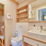 Badezimmer mit Dusche, Waschbecken und Toilette. Holzregale und Spiegel sind vorhanden.