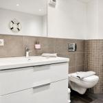 Bathroom with sink, mirror, and toilet. Walls covered with gray tiles.