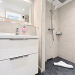 Bathroom with shower, sink, and mirror. Tile wall and white cabinet.