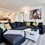 A living room with a large sofa, white coffee table, and kitchen area in the background.