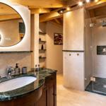 Badezimmer mit Dusche, Waschbecken und Spiegel. Holzdecken und Marmorflächen.