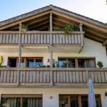 Haus mit zwei Balkonen, Holzverkleidung und Pflanzen. Umgeben von Bäumen.