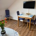 Dreisitzer-Tisch mit blauen Stühlen, Fernseher an der Wand, Tulpen im Vordergrund.