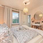 Bedroom with bed, window, mirror, and wall covering with plant motif.
