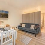 Living and dining area with sofa, table, and TV. Wooden floor and wall cladding.