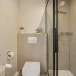 Bathroom with shower, toilet, and window. Shower base with glass wall and handheld shower.