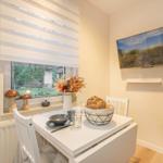 Dining room with table, chairs, and window view. Wall art and floral arrangement.