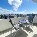 Terrasse mit Tisch und zwei Stühlen, Blick auf Wohngebiet unter blauem Himmel.