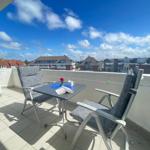 Terrasse mit Tisch und zwei Stühlen. Blick auf Wohngebiet unter blauem Himmel.
