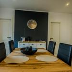 Dining room with wooden table, black chairs, and dark wall with clock.