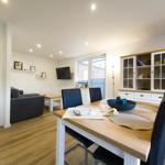 Dining area with wooden table and black chairs. Living area with sofa and TV in background.