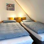 Zwei Einzelbetten mit Holzgestell und blauen Bettwäsche unter schräger Decke.