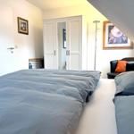 Schlafzimmer mit Doppelbett, Kleiderschrank und Sessel unter Dachschrägen.