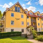 Gelbes Mehrfamilienhaus mit Balkonen und rotem Dach unter blauem Himmel.