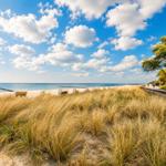 Strand mit Dünen, Strandkörben und blauem Himmel mit weißen Wolken.