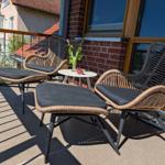 Terrasse mit zwei Rattan-Stühlen, Fußhocker und kleinem Tisch mit Blumen.