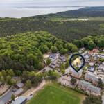 Luftbild einer Wohngegend mit Wald und Meer im Hintergrund. Ein markanter Punkt zeigt die Ferienwohnung.