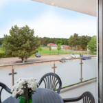Balkon mit Tisch und Stühlen, Blick auf Parkplatz und Grünfläche.