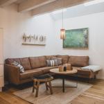 Ein Wohnzimmer mit braunem Sofa, Holzboden und Deckenbalken. An der Wand hängt ein Bild.