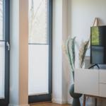 Ein Raum mit Holzboden, Fenster mit Jalousien und einem weißen Sideboard mit Pflanzen.