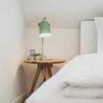 Schlafzimmer mit weißem Bett, Holztisch und grüner Lampe