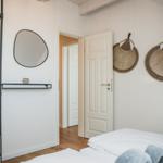 Schlafzimmer mit weißem Bett, Wandspiegel und zwei Wandkörben.