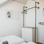 Schlafzimmer mit Bett, Kleiderständer und Deckenlicht. Wandbilder und Holzboden.