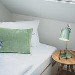 Ein Bett mit weißer Bettwäsche, grünem Kissen und einer Lampe auf einem runden Tisch.