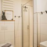 Badezimmer mit Dusche, Toilette und Waschbecken. Holzdecke und weiße Fliesen.