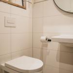Badezimmer mit Toilette, Waschbecken und Spiegel. Wandhalterung für Toilettenpapier.
