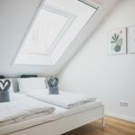 Schlafzimmer mit Dachfenster, Bett und Holzboden. Wandbilder und Lampe sind sichtbar.