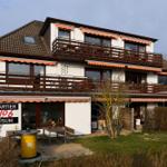 Zweistöckiges Haus mit Balkonen und Terrasse. Außenbereich mit Tischen und Sitzgelegenheiten.