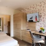 Schlafzimmer mit Bett, Schreibtisch und Fernseher an der Wand mit Blumenmotiv.
