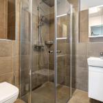 Bad mit Dusche, Waschbecken und Toilette. Fliesenwand und Spiegel.