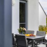 Terrasse mit Tisch, Stühlen und Obstschale. Hintergrund: Hauswand und Grünflächen.