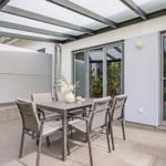 Terrasse mit Sitzgruppe unter Dach, Glasfront und Gartenbereich.