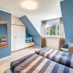 Zimmer mit zwei Betten, Kleiderschrank, Spiegel und Fenster mit Blick auf Außenbereich.