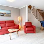 Wohn- und Essbereich mit rotem Sofa, Stuhl und Holztisch. Treppenhaus im Hintergrund.