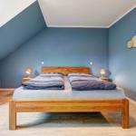 Doppelbett mit Holzrahmen, Nachttische und Sessel in einem Dachzimmer mit blauen Wänden.